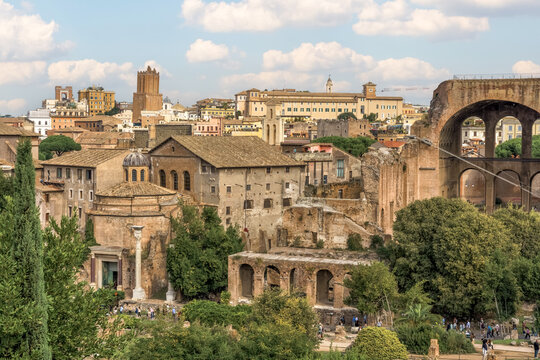 Panoramic view of the Roman Forum in Rome, Italy, featuring ancient ruins, historic buildings, and the massive arches of the Basilica of Maxentius under a bright sky.