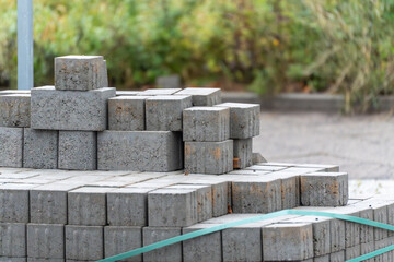 Stacked concrete paving blocks secured with a plastic strap at an outdoor worksite. Shallow depth of field and blurred greenery in the background.