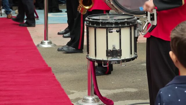 Detailed shot of a drummer's hands skillfully playing a snare drum in a lively procession. A military band showcases their talent at a formal event with a prestigious red carpet