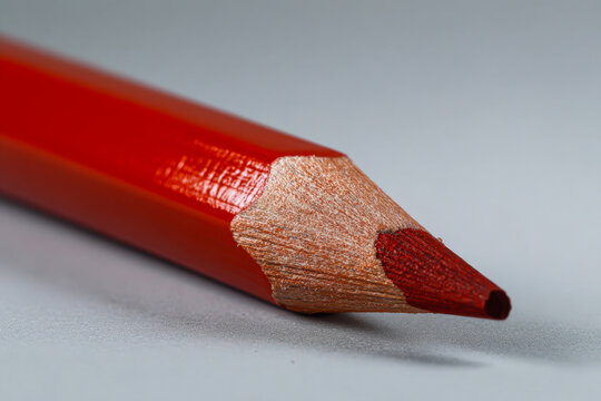 Detailed macro shot of a sharpened red colored pencil laying on a smooth gray surface showcasing wood texture and vibrant core pigment
