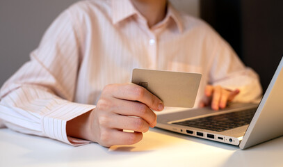 Close-up of a person holding a credit card while using a laptop, representing online shopping, digital payments, and secure internet transactions in a modern workspace