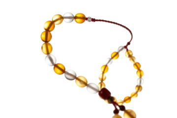 Elegant amber and clear beaded prayer beads (tasbih) with a red string and tassel, set against a transparent background. background removed