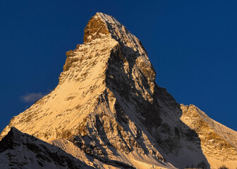 Scenic sunrise view of the Matterhorn rising between traditional Swiss alpine buildings in Zermatt, Switzerland. Morning light, winter season, peaceful mountain village atmosphere.
