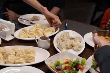 In a cozy setting, hands reach for steaming plates of dumplings and fresh salad as family members...