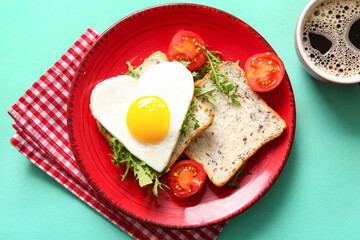 Plate with tasty fried egg, toasts, tomatoes, arugula and cup of coffee on turquoise background