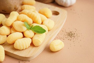 Wooden board with tasty gnocchi and basil on beige background, closeup