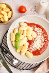 Plate and bowl of tasty gnocchi with tomato sauce and cheese on white background