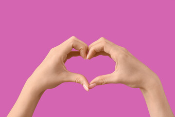 Fototapeta premium Female hands showing heart gesture on purple background. Valentine's Day celebration