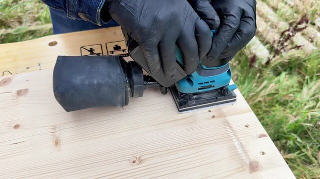 Professional man carpenter using electric sander to polish wood on rough workbench at back yard. Design, carpentry, craftsmanship and handwork concept. High quality 4k footage
