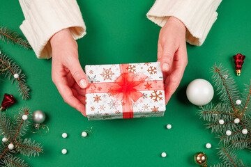 Woman's hands giving a beautifully wrapped Christmas present with a red bow. Green backdrop and...