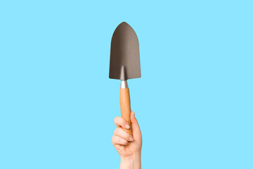 Female hand with gardening shovel on color background, closeup