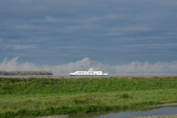 Bateau de transport fluvial naviguant sur un fleuve sous ciel nuageux