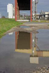 Réflexion d’une structure industrielle dans une flaque d’eau sur un chemin