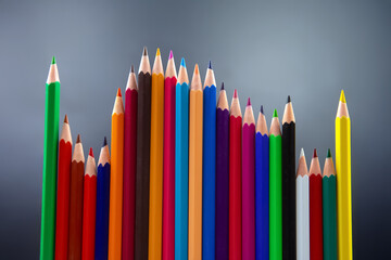 Fototapeta premium Brightly colored pencils in a symmetrical wave arrangement, set against a smooth gray backdrop. Perfect for promoting art supplies, education, or creative inspiration themes.
