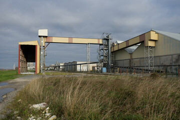Site industriel avec bâtiments métalliques et structure de convoyeur extérieur