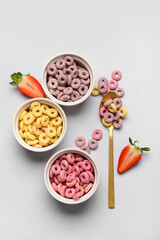 Bowls with colorful sweet cereal rings and cut strawberry on grey background