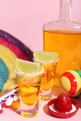 Bottle of tequila, shots, lime and maracas on yellow background, closeup