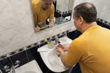 Washing hands under running water before brushing teeth, caucasian adult male preparing for oral hygiene at home sink. Man Brushing Teeth