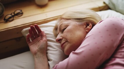Blond senior woman lying on orthopedic pillow, enjoying healthy morning sleep