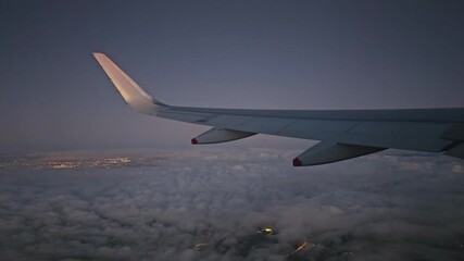 Airplane window showing the wing flying over city lights and clouds at night, 4k resolution footage - Powered by Adobe