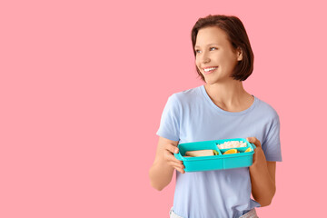 Beautiful young happy woman with lunchbox of tasty food on pink background