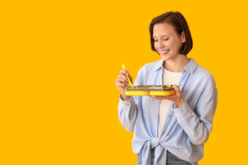Beautiful young happy woman with lunchbox of tasty food on yellow background