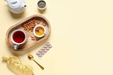 Sleep mask, pills and tea set with wooden tray on beige background