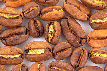 Close-up of roasted coffee beans with rich brown hues, showcasing their textured surfaces and natural splits on a white background. Perfect for coffee-related themes.