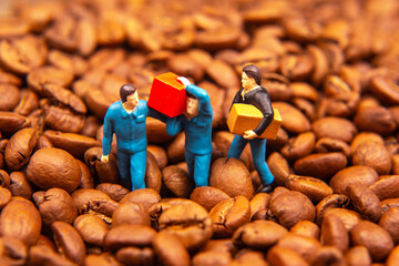 A creative close-up of three miniature figures in blue uniforms exchanging a yellow box and a red package amidst a sea of coffee beans, symbolizing trade or commerce. 
