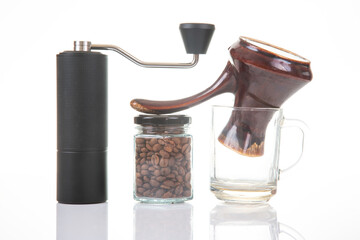 A modern black manual grinder, a glass jar of coffee beans, and a traditional ceramic cezve on a white backdrop, ideal for showcasing coffee preparation tools.