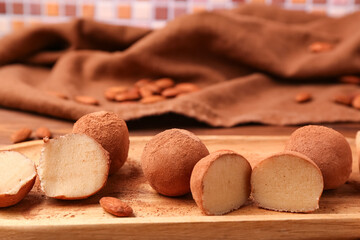 Board with tasty marzipan candies covered with cocoa powder on table, closeup