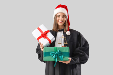 Female judge in Santa hat with Christmas presents on light background