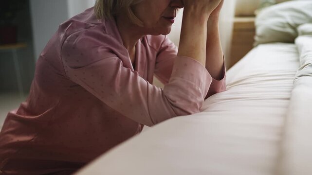 Senior woman in pajamas praying before bed in morning, hoping for better health