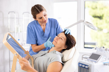 Obraz premium Woman beautician examining face skin of female patient before cosmetology procedure in beauty clinic
