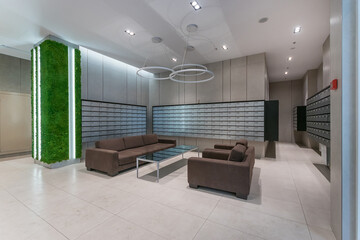 In a contemporary lobby, comfortable couches surround a glass table. Sleek mailboxes line the...