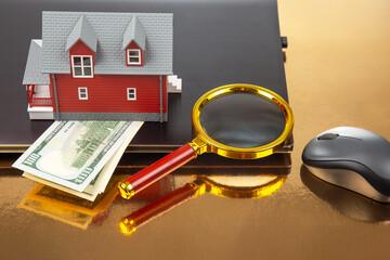 Finding and buying a home over the Internet. House model on the background of a laptop and a magnifying glass.