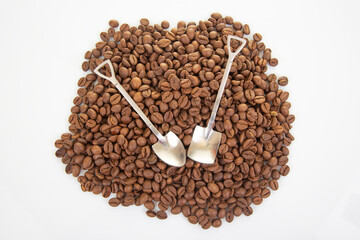 Close-up of intersecting stainless steel shovels on a textured layer of dark roasted coffee beans, perfect for culinary or agricultural stock imagery