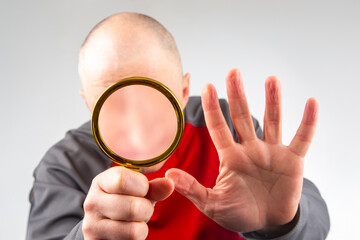 man hides his face with a magnifying glass. The concept of searching for a person in a database. Look at the world incognito. anonymous behind the curtain