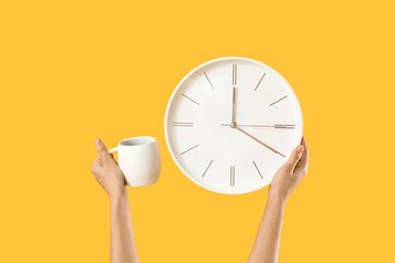 Female hands with clock and cup of coffee on yellow background