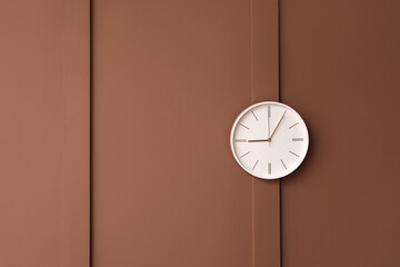 Stylish clock hanging on brown wall