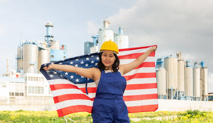 Cheerful asian female worker in hardhat with american flag standing in front of factory