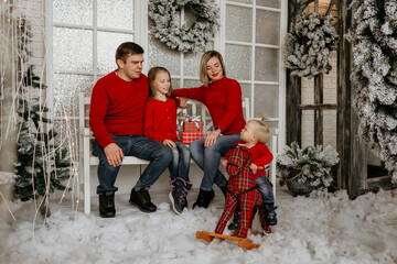 A little toddler standing in faux snow next to a rocking horse, with their family sitting and smiling on a bench in the background