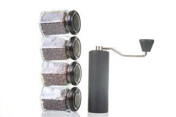 black manual coffee grinder for coffee beans and four glass transparent jars with black lids filled with roasted coffee beans and earthenware for brewing coffee on a white background.