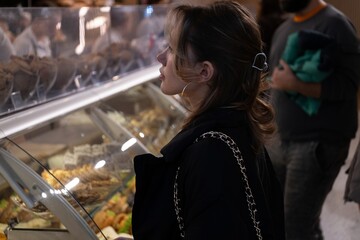 Young woman examines a bakery display case while deciding what to buy.