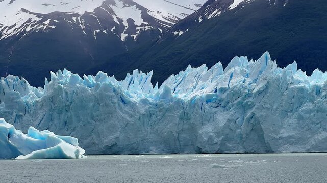 The glacier on Lake Argentino in Patagonia, Argentina, stands before snowy mountain peaks near Perito Moreno, showing bright blue ice and striking natural beauty.