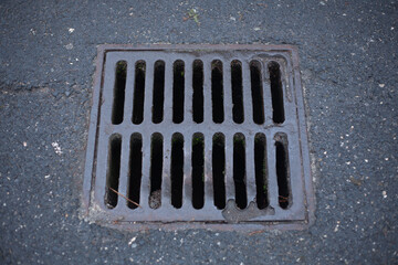 Metal storm drain grate embedded in asphalt pavement, showing weathered texture and urban infrastructure detail
