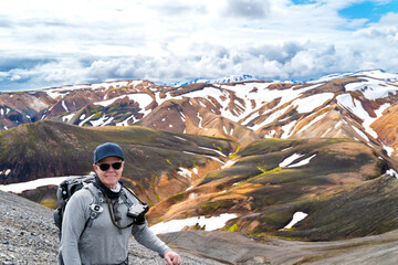 Iceland travel: Portrait of a Senior man looking at camera at Landmannalaugar Fjallabak Nature Reserve Central Iceland from the top of a mountain in summer