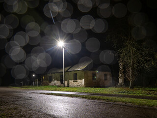 Night street scene with an old abandoned building illuminated by a streetlamp, with rain bokeh creating atmospheric, moody light effects