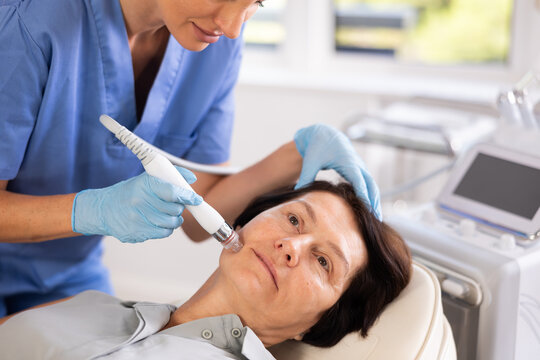 Elderly woman getting facial deep hydration procedure from experienced cosmetologist in aesthetic medicine office