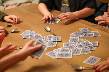 Group of people playing the fun, popular and competitive card game spoons on the dining room table. 